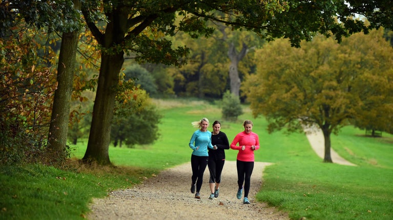 Three people running on a path through woodland